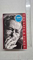 Front cover of the book showing black-and-white close-up photo of a man smoking a cigarette, with title 'The Life & Times' and blue sticker indicating 'signed by author'.