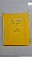 Front cover of a yellow hardcover book with gold embossed text 'The National Geographic Society 100 Years of Adventure and Discovery'.