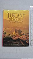 Front cover of the cookbook featuring a scenic Tuscan landscape and pottery dishes under clear title text.