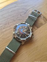 Front view of watch flat on wooden surface showing full case, bezel, dial and strap