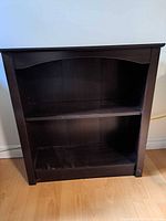 Single wood bookshelf stained dark brown, showing front view with slightly arched top and center shelf installed.