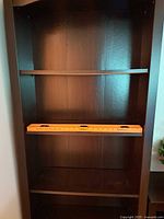 Close-up of middle and bottom shelves, showing dark brown stained wood and fixed middle shelf with one adjustable shelf above.