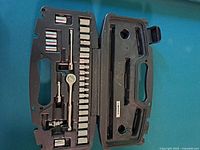 Open case showing ratchet wrench, assorted sockets, extension bar, and universal joint arranged in molded plastic slots inside black hard plastic case.
