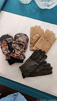 Image showing all three pairs of gloves laid out: camo convertible mittens, light brown suede gloves, and dark brown leather gloves, all appearing new and unworn.