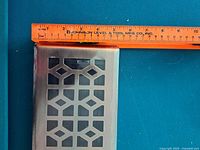 Close-up image of the bronze metal vent cover showing the detailed geometric cutout pattern with a ruler indicating size.