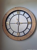 Full front view of the large round clock mounted on wall, showing the wood outer frame and metal center with Roman numerals and brass hands.