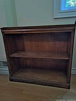 Front view of one Sauder brand bookshelf showing solid wood construction, one adjustable shelf, stained antique walnut color.