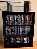 Full view of three rows of VHS tapes labeled Star Trek original series, arranged on black shelf, with some tapes above shelf