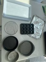 Photo showing one small muffin tray, three round baking pans, one rectangular baking pan, two trays (one with foil), and one cooling rack