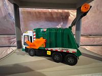 Side view of the green recycling truck toy showing the orange lifting arm and six wheels.