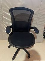 Photo of black ergonomic computer chair with mesh back and padded seat on a wheeled base