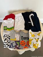 Photo of five boys' t-shirts with various prints and three pairs of shorts in white, black, and navy blue colors.
