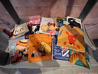 Variety of eleven hardcover children's books arranged side by side on a surface, visible titles and colorful cartoon-style covers