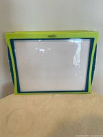 Photo showing a rectangular Etch and Sketch toy with green and blue frame and a clear drawing screen.