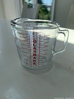 Clear glass measuring cup with red measurement markings up to 950 ml, visible handle and spout, placed on white surface with background