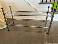 Front side view showing two-tier shoe rack with metal wire mesh shelves and tubular metal legs capped in black.