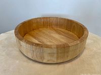 Large wooden mixing bowl on neutral surface, showing round shape and wood grain detail.