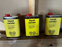 Photo of three yellow litres cans of Cira 1850 Liquid Sander, each with red caps and bold text detailing the product's uses and hazards.