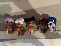Five LOL Surprise dolls arranged in a line showing their front view with various hair colors and styles, one doll in an animal costume