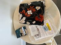 Folded king size duvet cover with floral pattern in dark, white, and reddish-orange colors, displayed on a round light chair.