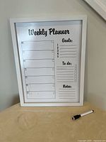 Photo of a weekly planner whiteboard with sections for days of the week, goals, to-do list, and notes. Includes one black dry erase marker.