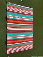 Photo of a rectangular outdoor plastic mat with colourful horizontal stripes in red, green, white and orange.