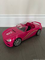 Photo of the front and side view of a pink Barbie convertible toy car with a black interior and decorative decals.
