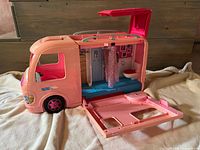 Pink Barbie motor home side view with side door open showing detailed interior including seating and bathroom fixtures.