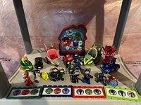 Shows a variety of PJ Mask toys arranged on a flat surface including figures, vehicles, and character tokens.