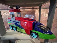 Multi-colored PJ Masks large vehicle with blue, green, red panels and light blue wheels on a shelf.