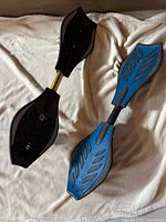 Two Razor Ripstick caster boards, one black with gold, one blue with black, laid out to show top side with deck and grip details.