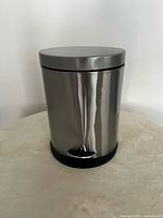 Closed view of the small stainless steel garbage pail showing polished finish and black base.