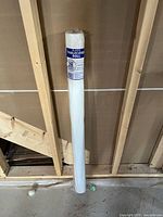 Photo of unopened white banquet tablecloth roll standing upright against a wall, showing label indicating coverage for 28 tables.