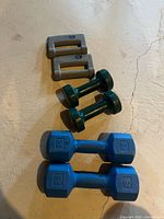 Photo showing three pairs of dumbbells in gray, green, and blue colors on concrete floor.