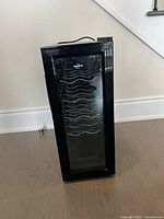 Front view of the black wine cellar with a glass door and metal racks for bottle storage.