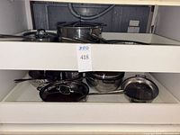 Two white drawers open, revealing multiple stainless steel pots, skillets, sauté pan and lids