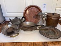 Copper and brass assorted kitchenware including a hammered copper tray, brass teapot, double boiler pan, ladle, small melting pots, and a fluted platter.
