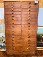 Full front view of tall oak cabinet showing 29 drawers and wood knobs