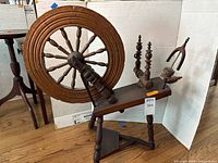 Full view of antique wooden spinning wheel showing large wheel with turned spokes and mounted on tripod legs with treadle pedal.