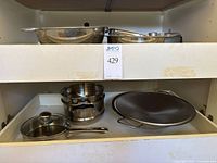 Drawer with multiple stainless steel pots, lids, strainers, and pans stacked and arranged.