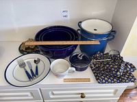 Full lot display showing large blue Le Creuset stock pot with steamer basket, Chantal blue saucepan with lid, white plate with blue rim, child's flatware set, coffee mug, mixing bowls, and trivets.