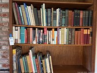Full bookshelf view with three shelves showing assorted hardcover and paperback books on religious and historical subjects.