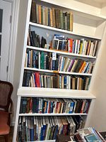 Four-tier white bookshelf holding assorted books from floor to near ceiling