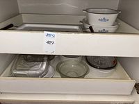 Shelf with various clear glass and corningware dishes, some covered and some uncovered.