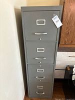 Front view of a gray metal filing cabinet with four drawers, each drawer has a handle and label holder