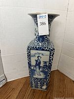 Full view of the tall blue and white porcelain vase showing one scenic side with a female figure next to a railing and foliage.