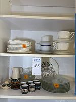 Porcelain luncheon plates stacked and white porcelain cups with some saucers on shelf