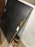 Photo of laser table standing upright showing pegboard surface and metal frame with label on corner.