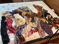 Overview of 17 assorted scarves laid out on mattress, showing a variety of patterns and colors including floral, geometric, and abstract.