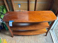 Full view of wooden console table with two open shelves, curved front, and positioned on wooden floor in a garage or storage area.